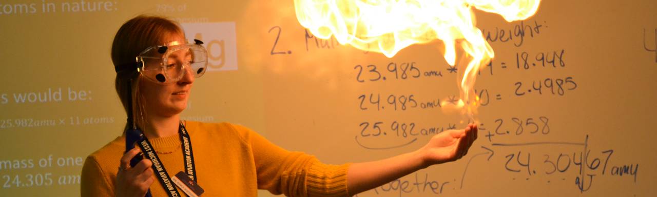 A teacher displays a chemical reaction by creating a small fireball above her outstretched hand.